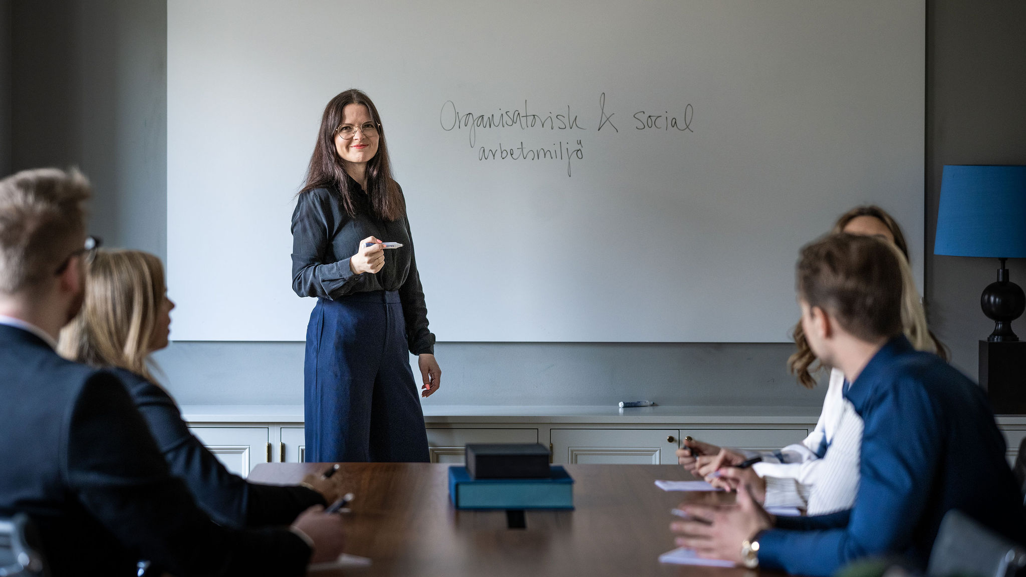 Kvinna presenterar vid whiteboard inför lyssnande kollegor.